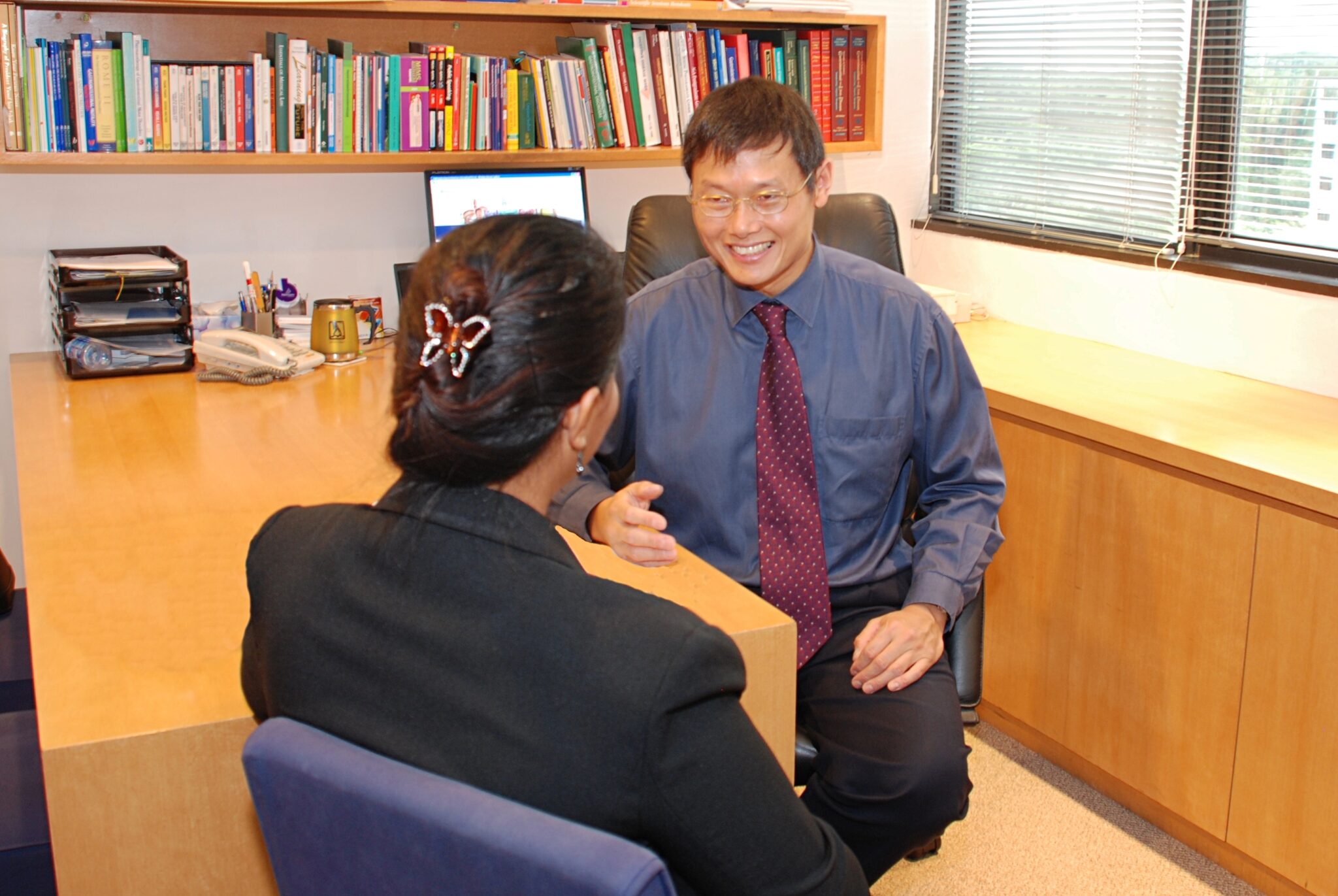 Dr Tan Chi Chiu smiling during a coaching session in his office, talking with a client across a desk